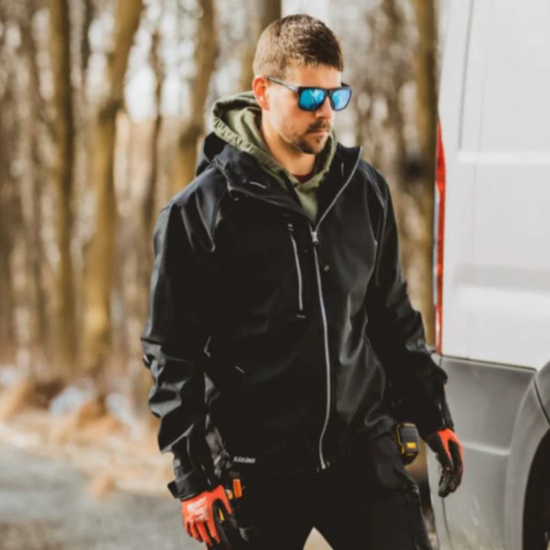 Man in workwear and sunglasses standing next to a white van in a forest setting